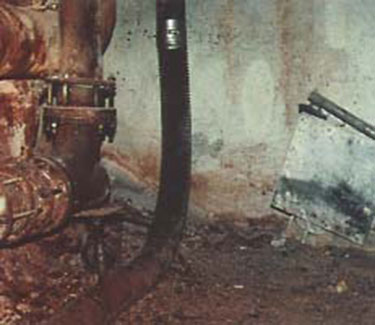 Old ceramic, refractory-type elbow is shown above. Material blown out from frequent plug-ups can still be seen on the floor and pipes.